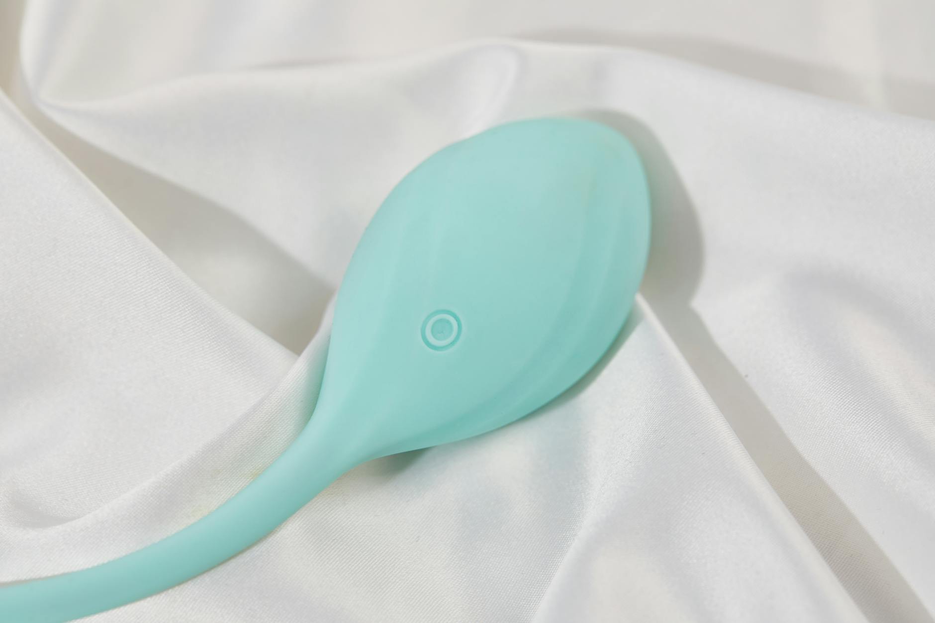 A stylish teal vibrator on smooth white silk fabric, showcasing the elegant design of modern lemon adult toys.