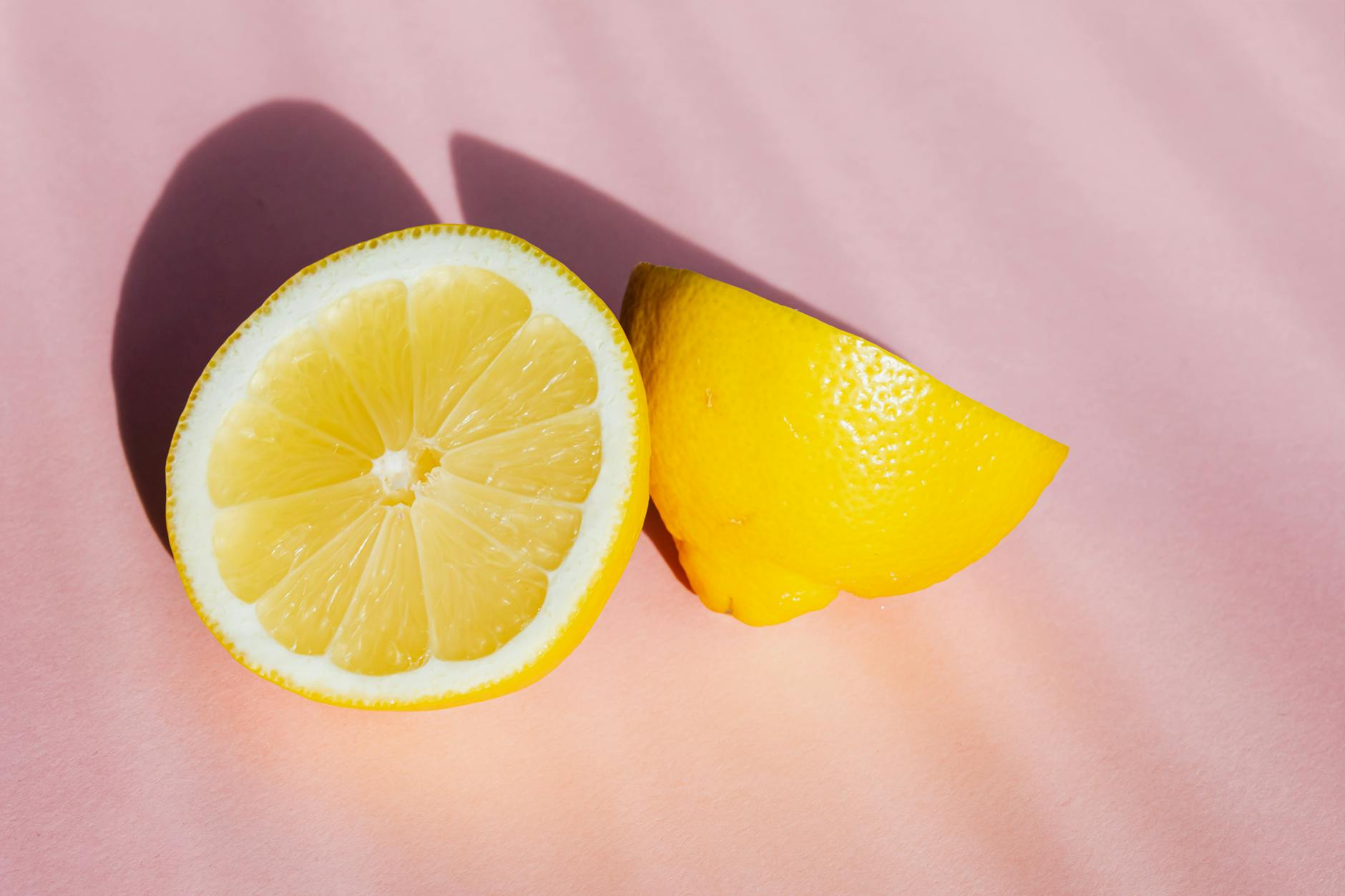 Fresh lemon halves on a pink background with sunlight, symbolizing the fresh and approachable design of lemon clitoral vibrators