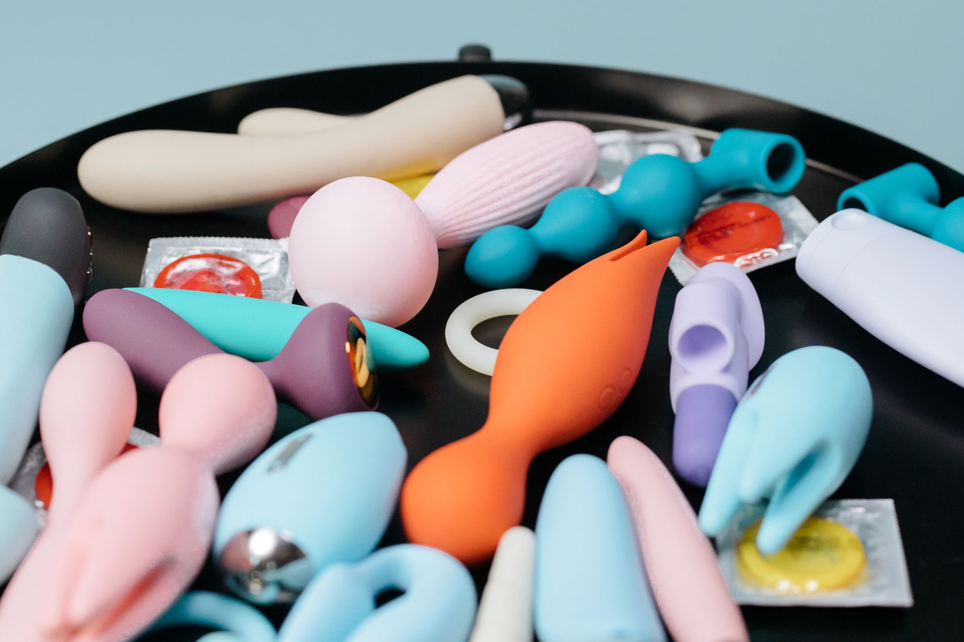 Woman holding blue and pink silicone vibrators thoughtfully, representing options for sensitive tissue pleasure