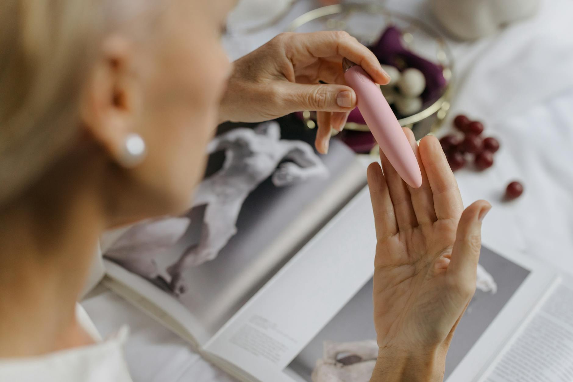 Close-up of a woman holding a pink vibrator with art books nearby, emphasizing intimate reconnection with the body