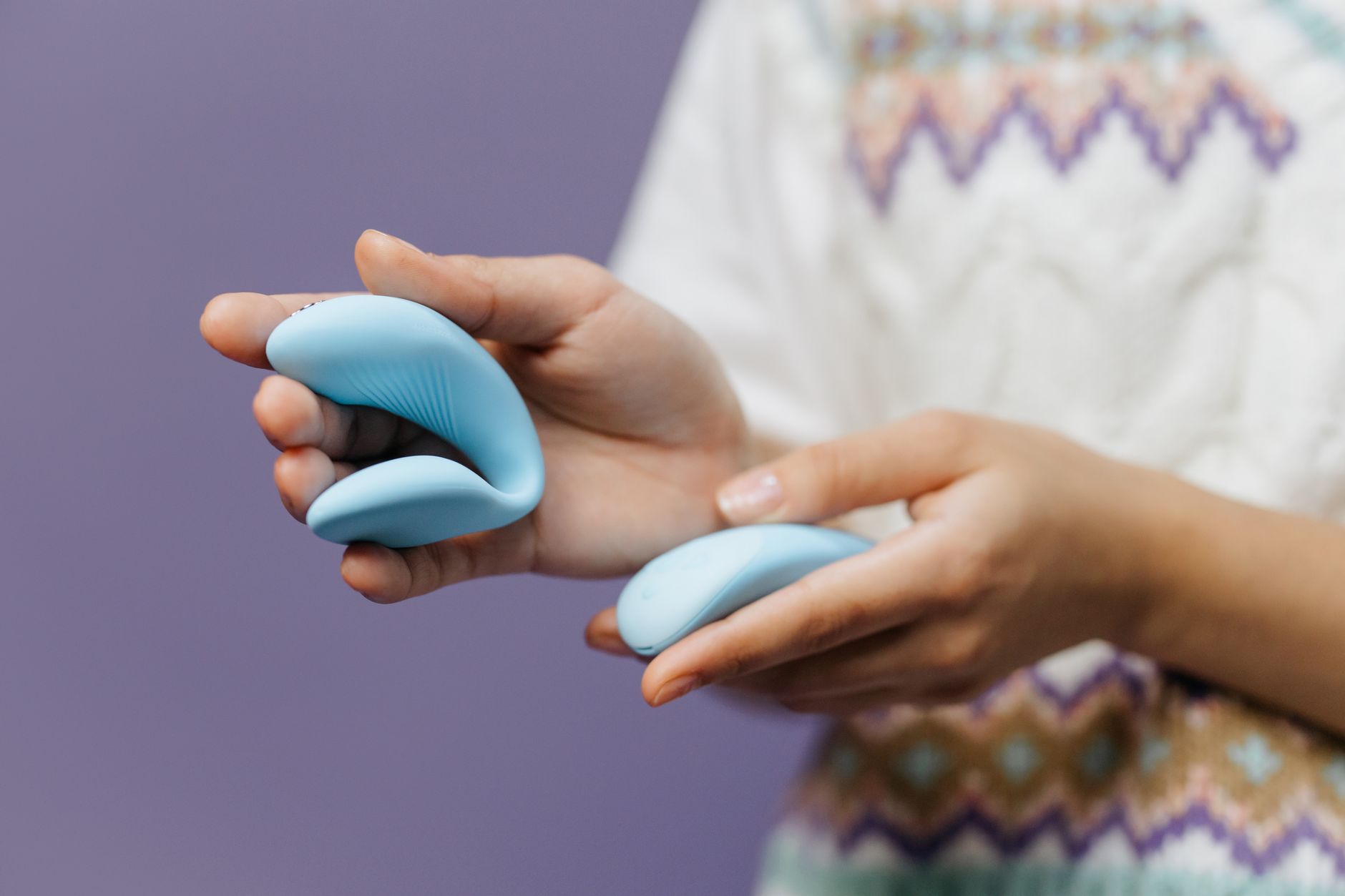 A blue silicone clitoral vibrator held in hand against a solid background, promoting self-care and pleasure