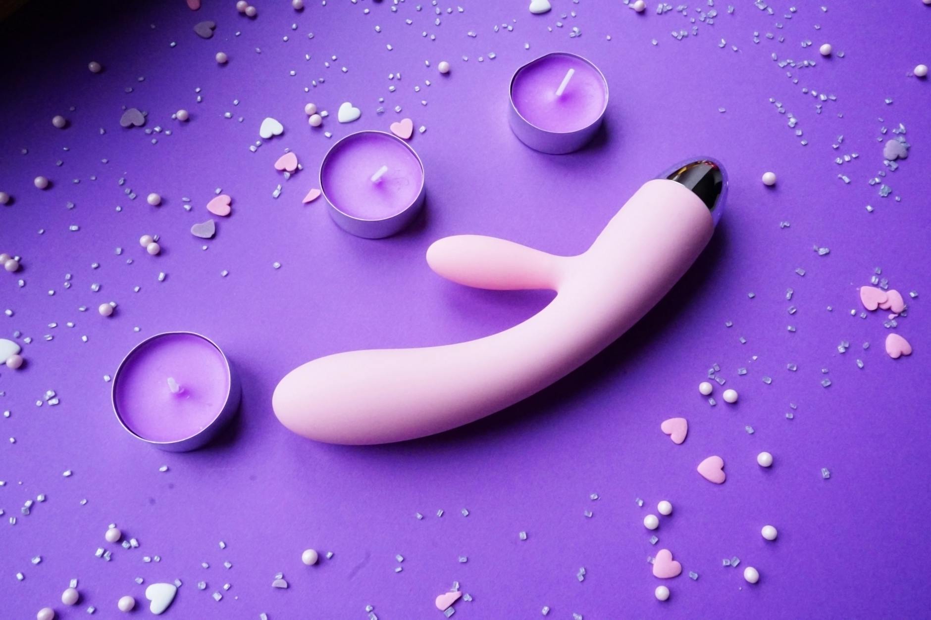 Pink vibrator on purple background with hearts and candles for romantic moments